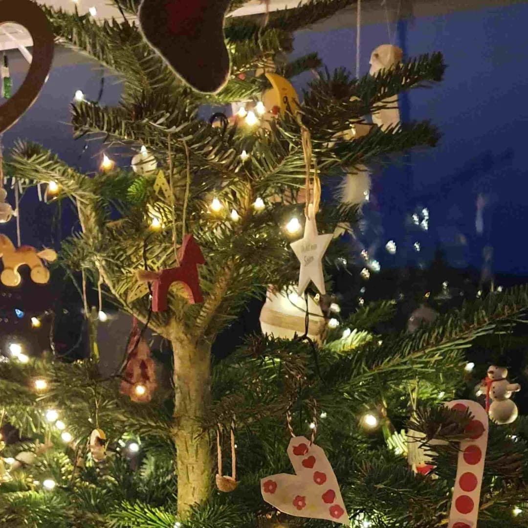 Geschmückter Weihnachtsbaum mit Lichterkette, Holzfiguren und selbstgebastelten Anhängern vor dunkelblauer Wand